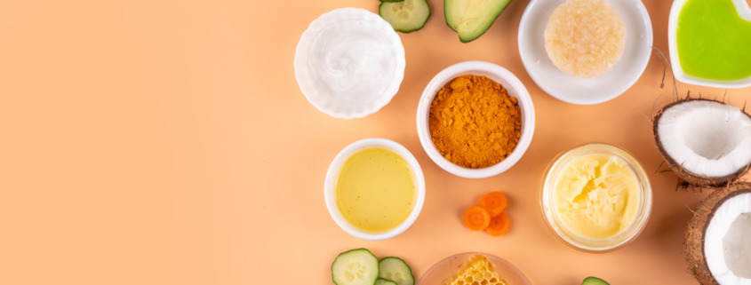 Zutaten für DIY Sonnenlotion mit Avocado, Kokosöl, Kurkuma, Honig und Gurke auf hellem Hintergrund.